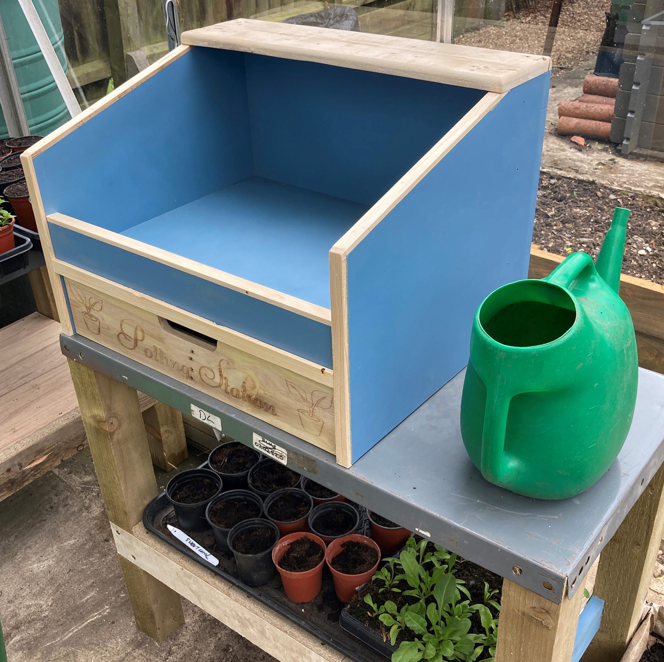 A blue potting station with a green watering can. Links to the corresponding product page